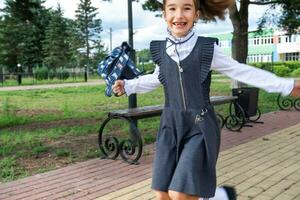 alegre gracioso niña con sin dientes sonrisa en colegio uniforme con blanco arcos corriendo en colegio patio trasero. espalda a escuela, septiembre 1. contento alumno con mochila. primario educación, elemental clase. movimiento foto