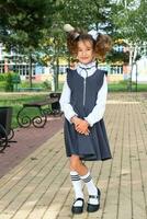 Cheerful funny girl with a toothless smile in a school uniform with white bows in school yard. Back to school, September 1. A happy pupil. Primary education, elementary class. Portrait of a student photo