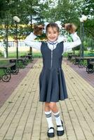 alegre gracioso niña con un sin dientes sonrisa en un colegio uniforme con blanco arcos en colegio patio trasero. espalda a escuela, septiembre 1. un contento alumno. primario educación, elemental clase. retrato de un estudiante foto