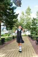 Cheerful funny girl with toothless smile in school uniform with white bows in school yard tosses the backpack. Back to school, September 1. Happy pupil. Primary education, elementary class. photo