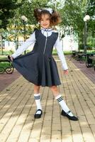 Cheerful funny girl with a toothless smile in a school uniform with white bows in school yard. Back to school, September 1. A happy pupil. Primary education, elementary class. Portrait of a student photo