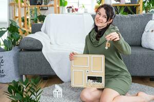 Happy woman in house holds in hands photo frame with figure at home template and key in interior. Dream house project, real estate purchase, insurance, mortgage, rent, reservation