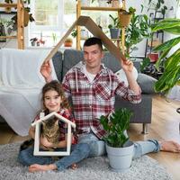 Incomplete family dad and daughter and pet cat are enjoying new home, sitting on sofa. Mortgage, insurance and protection, buying and moving into your own home, green house with potted plant photo