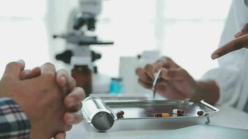 medizinisch Arbeiter im Labor Mantel und steril Maske, tun ein Mikroskop Analyse während ihr Kollege sind Arbeiten hinter video