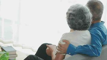 Happy senior couple using remote control to change channel. Seniors watch TV for entertainment while man using remote control. Wife and old man sitting on couch in living room with television show. video