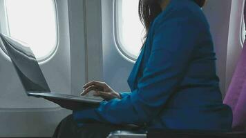 Successful beautiful young asian business woman sits in airplane cabinplane and works on digital tablet with stylus. Flying at first class. video