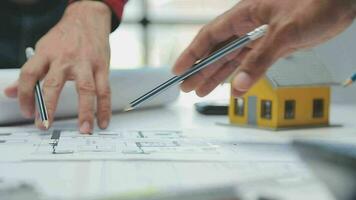 team van multi-etnisch architecten werken Aan bouw plannen in vergadering kamer. ingenieurs bespreken Aan project in kantoor. volwassen zakenman en vrouw staand in de omgeving van tafel werken Aan blauwdruk. video