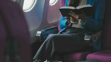 bem sucedido fêmea livro editor lendo literatura durante Tempo dentro avião antes o negócio encontro com escritor, confiante formalmente vestido mulher desfrutando internacional voar e lazer para romance video