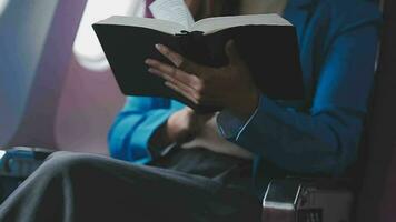 exitoso hembra libro editor leyendo literatura durante hora en avión antes de negocio reunión con escritor, confidente formalmente vestido mujer disfrutando internacional vuelo y ocio para novela video