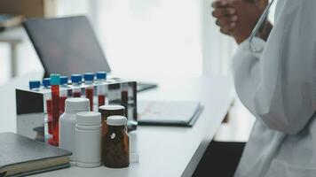 Medical worker in lab coat and sterile mask, doing a microscope analysis while her colleague are working behind video