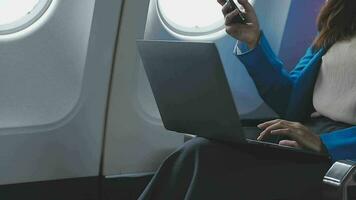 Successful beautiful young asian business woman sits in airplane cabinplane and works on digital tablet with stylus. Flying at first class. video