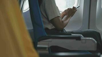 Businesswoman with short haircut sitting in airplane cabin and chatting online on smartphone while checking email on laptop computer with mock up area.Female traveler reading notification on cellular video