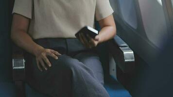 Businesswoman with short haircut sitting in airplane cabin and chatting online on smartphone while checking email on laptop computer with mock up area.Female traveler reading notification on cellular video