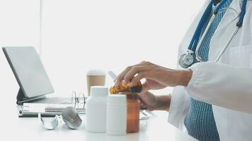 Medical worker in lab coat and sterile mask, doing a microscope analysis while her colleague are working behind video