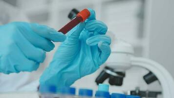 Medical worker in lab coat and sterile mask, doing a microscope analysis while her colleague are working behind video