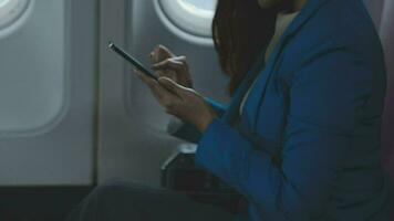 in viaggio e tecnologia. volante a primo classe. bella giovane imprenditori donna utilizzando smartphone mentre seduta nel aereo. video