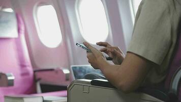 mujer de negocios con corto Corte de pelo sentado en avión cabina y chateando en línea en teléfono inteligente mientras comprobación correo electrónico en ordenador portátil computadora con burlarse de arriba zona.femenina viajero leyendo notificación en celular video