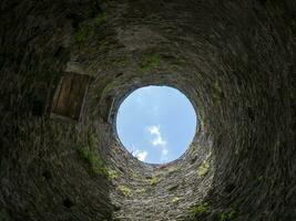 Stone well hole, old construction from inside, brick walls and blue sky background, fall down in the well concept photo