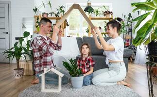 tradicional familia con niño son disfrutando nuevo hogar, sentado en el sofá y participación el techo. hipoteca, seguro y proteccion, comprando y Moviente dentro tu propio hogar, verde casa con en conserva planta foto