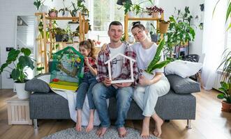 traditional family with a child and a parrot pet in a cage are enjoying a new home, sitting on the sofa and holding the roof. Mortgage, insurance, buying and moving into your own home photo