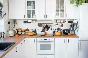 Decor of the white classic kitchen with pumpkins for Halloween and harvest. Autumn mood in the home interior, modern loft style. photo