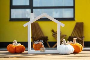 Autumn decor on porch of yellow house outside of pumpkin, lantern, garlands and figure of home and key. Halloween party, autumn mood, Harvest festival, real estate, insurance, mortgage photo