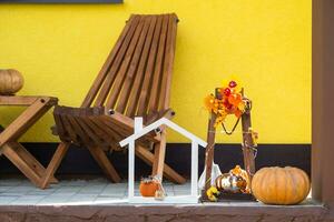 Autumn decor on porch of yellow house outside of pumpkin, lantern, garlands and figure of home and key. Halloween party, autumn mood, Harvest festival, real estate, insurance, mortgage photo