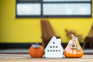 Autumn decor on porch of yellow house outside of pumpkin, lantern, garlands and figure of home and key. Halloween party, autumn mood, Harvest festival, real estate, insurance, mortgage photo