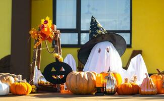 Child in bed sheet with slits like ghost in witch's hat and Halloween decor on the porch of the house outside in the yard of pumpkin, lantern, garlands, ack lantern. party, autumn mood photo