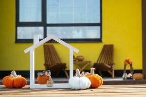 Autumn decor on porch of yellow house outside of pumpkin, lantern, garlands and figure of home and key. Halloween party, autumn mood, Harvest festival, real estate, insurance, mortgage photo