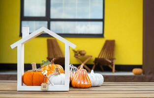 Autumn decor on porch of yellow house outside of pumpkin, lantern, garlands and figure of home and key. Halloween party, autumn mood, Harvest festival, real estate, insurance, mortgage photo