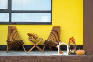 Autumn decor on porch of yellow house outside of pumpkin, lantern, garlands and figure of home and key. Halloween party, autumn mood, Harvest festival, real estate, insurance, mortgage photo