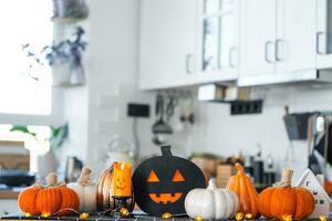 Decor of white classic kitchen with pumpkins, garlands, jack latern for Halloween and harvest with figurine of house. Autumn mood in home interior, modern loft style. real estate, insurance, mortgage photo