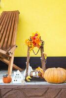 Autumn decor on porch of yellow house outside of pumpkin, lantern, garlands and figure of home and key. Halloween party, autumn mood, Harvest festival, real estate, insurance, mortgage photo