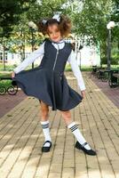 Cheerful funny girl with a toothless smile in a school uniform with white bows in school yard. Back to school, September 1. A happy pupil. Primary education, elementary class. Portrait of a student photo