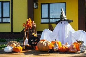 niño en cama sábana con hendiduras me gusta fantasma en de bruja sombrero y Víspera de Todos los Santos decoración en el porche de el casa fuera de en el yarda de calabaza, linterna, guirnaldas, ack linterna. fiesta, otoño estado animico foto