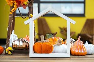 Autumn decor on porch of yellow house outside of pumpkin, lantern, garlands and figure of home and key. Halloween party, autumn mood, Harvest festival, real estate, insurance, mortgage photo