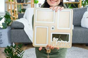 Happy woman in house holds in hands photo frame with figure at home template and key in interior. Dream house project, real estate purchase, insurance, mortgage, rent, reservation