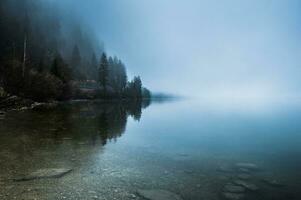 Foggy morning on the border of calm lake in Austrian Alps photo