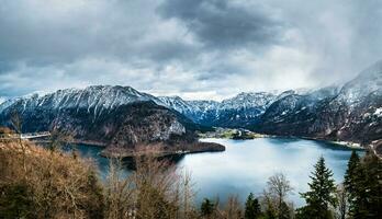 panorama de austriaco Alpes cubierto con nieve con un hermosa calma lago y nublado cielo en el antecedentes foto