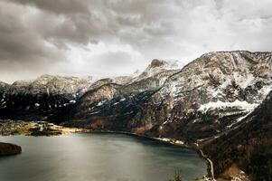 austriaco Alpes cubierto con nieve con un hermosa calma lago y nublado cielo en el antecedentes foto