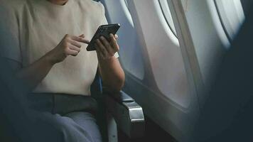 Businesswoman with short haircut sitting in airplane cabin and chatting online on smartphone while checking email on laptop computer with mock up area.Female traveler reading notification on cellular video