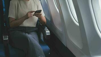 mujer de negocios con corto Corte de pelo sentado en avión cabina y chateando en línea en teléfono inteligente mientras comprobación correo electrónico en ordenador portátil computadora con burlarse de arriba zona.femenina viajero leyendo notificación en celular video