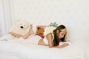 Cute Caucasian teen girl reads her diary sitting on the bed in sleeping clothes and makes notes in it photo