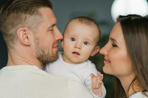 Happy young parents hold their little son in their arms and smile happily looking at him photo