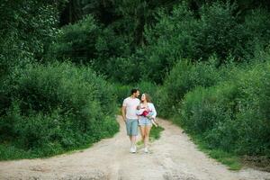 A happy young family with their son in their arms are walking along a forest path and enjoying the summer weather photo