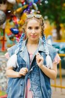 Young woman with blue pigtails in a denim vest in an amusement park photo