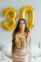 Cute Caucasian girl in a nightgown, who is congratulated on her birthday in bed, blows out a candle on a cake and makes a wish for a celebration, lifestyle and holiday concept. photo