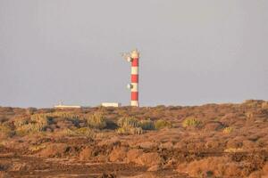 un faro en un colina con un rojo y blanco torre foto