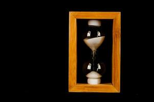 un reloj de arena en un de madera caja en un negro antecedentes foto